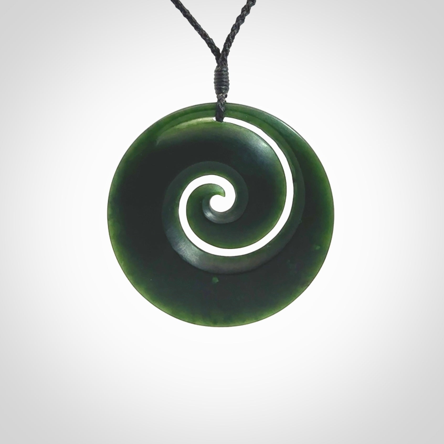 This is a large deep and dark green New Zealand jade koru pendant. We have bound this with a black coloured cord necklace. The necklace is adjustable so you can position the piece where it suits you the best. Hand made by Ric Moor.