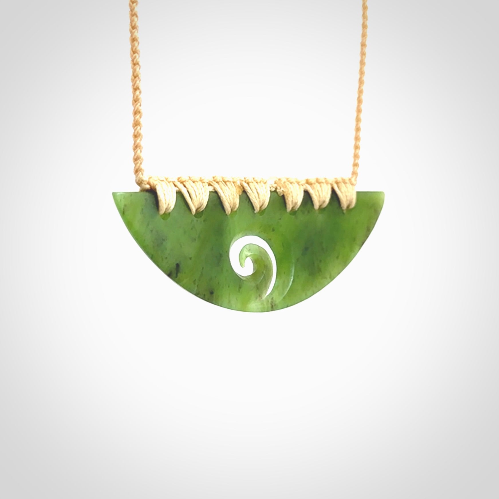 This picture shows a hand carved jade half-shield with Koru pendant. It is a semi-translucent green colour. This is a wonderful piece of jewellery. The cord is hand plaited and adjustable so that you can position the pendant where it suits you best. This piece was carved for us by Ric Moor. Delivery is free worldwide.