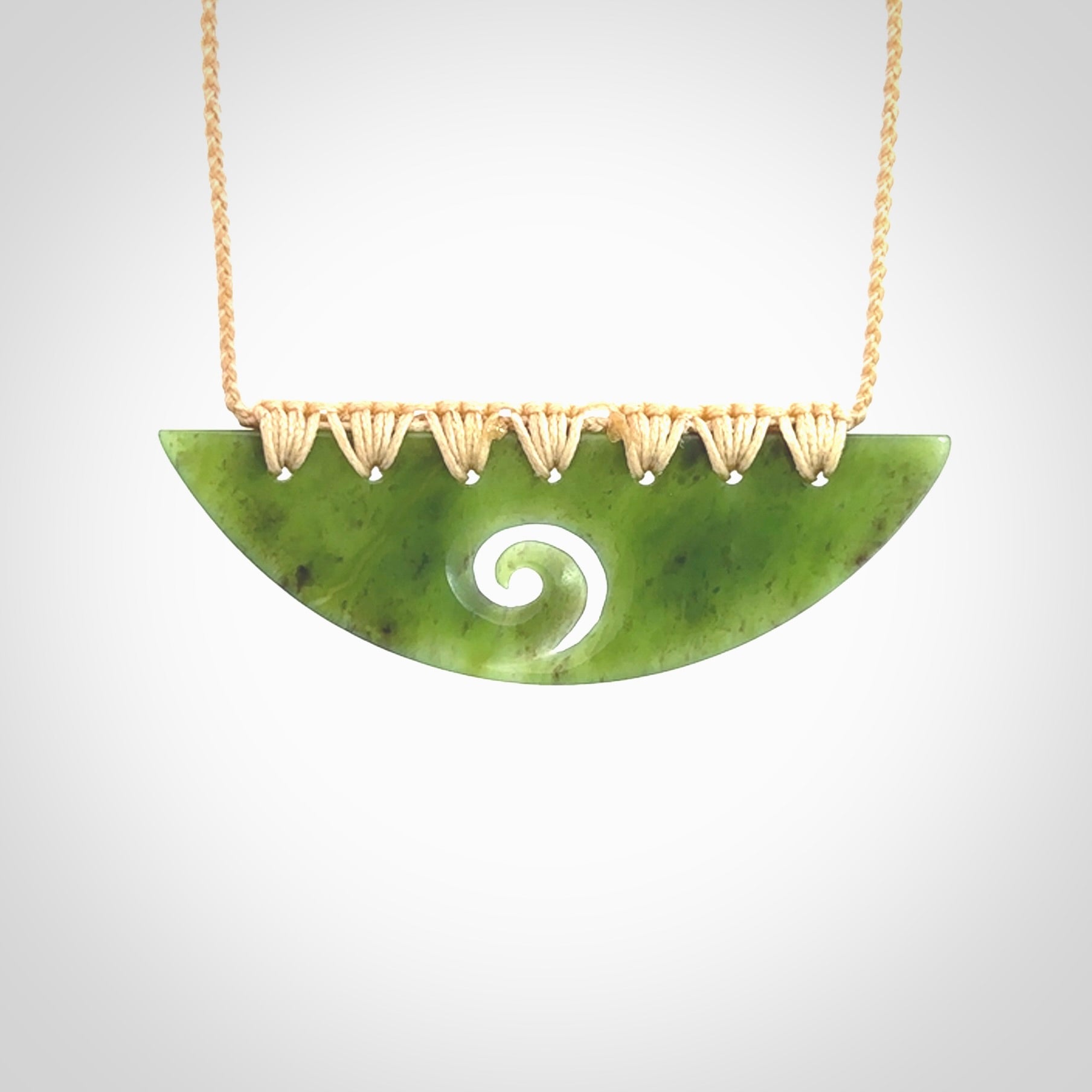 This picture shows a hand carved jade half-shield with Koru pendant. It is a semi-translucent green colour. This is a wonderful piece of jewellery. The cord is hand plaited and adjustable so that you can position the pendant where it suits you best. This piece was carved for us by Ric Moor. Delivery is free worldwide.