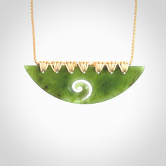 This picture shows a hand carved jade half-shield with Koru pendant. It is a semi-translucent green colour. This is a wonderful piece of jewellery. The cord is hand plaited and adjustable so that you can position the pendant where it suits you best. This piece was carved for us by Ric Moor. Delivery is free worldwide.