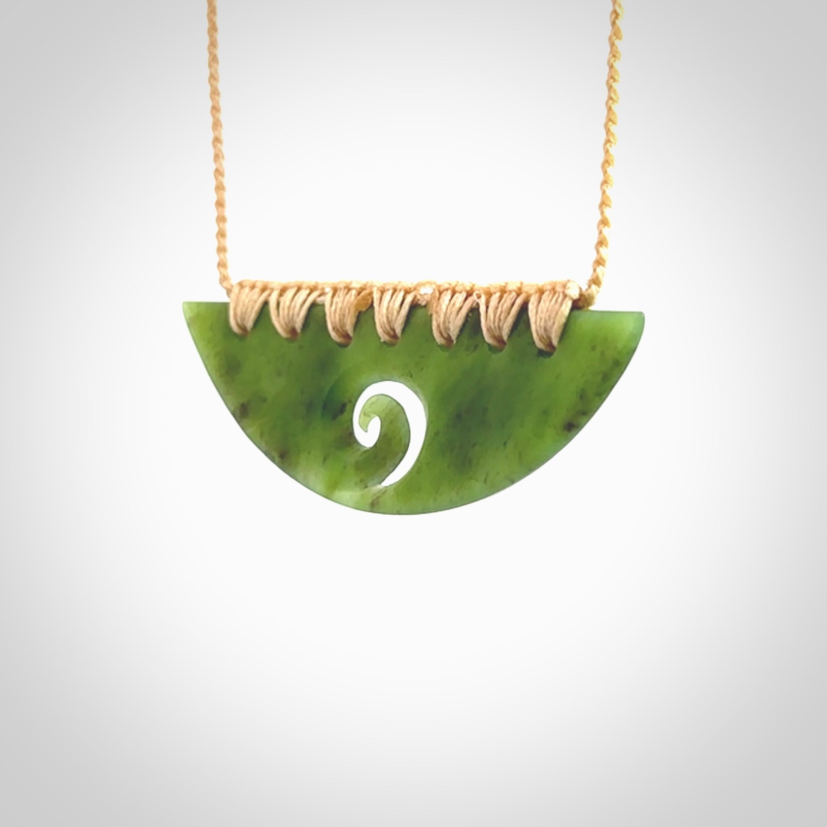 This picture shows a hand carved jade half-shield with Koru pendant. It is a semi-translucent green colour. This is a wonderful piece of jewellery. The cord is hand plaited and adjustable so that you can position the pendant where it suits you best. This piece was carved for us by Ric Moor. Delivery is free worldwide.