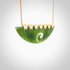 This picture shows a hand carved jade half-shield with Koru pendant. It is a semi-translucent green colour. This is a wonderful piece of jewellery. The cord is hand plaited and adjustable so that you can position the pendant where it suits you best. This piece was carved for us by Ric Moor. Delivery is free worldwide.