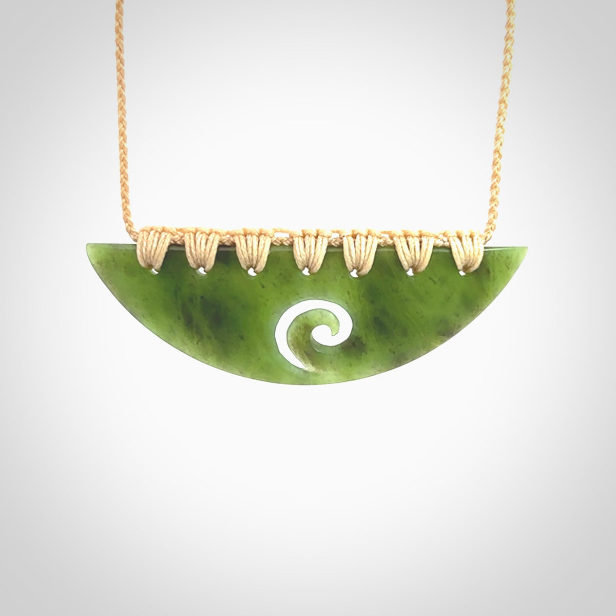 This picture shows a hand carved jade half-shield with Koru pendant. It is a semi-translucent green colour. This is a wonderful piece of jewellery. The cord is hand plaited and adjustable so that you can position the pendant where it suits you best. This piece was carved for us by Ric Moor. Delivery is free worldwide.