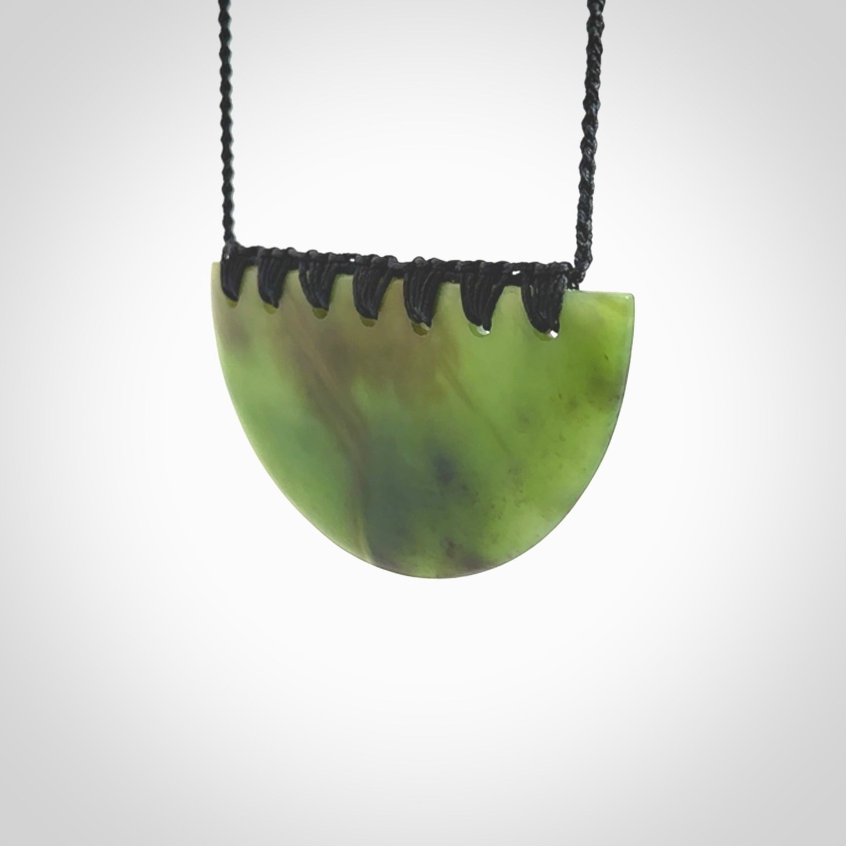 This picture shows a hand carved jade contemporary half-shield pendant. It is a deep green colour. This is a wonderful piece of jewellery. The cord is hand plaited and adjustable so that you can position the pendant where it suits you best. This piece was carved for us by Ric Moor. Delivery is free worldwide.