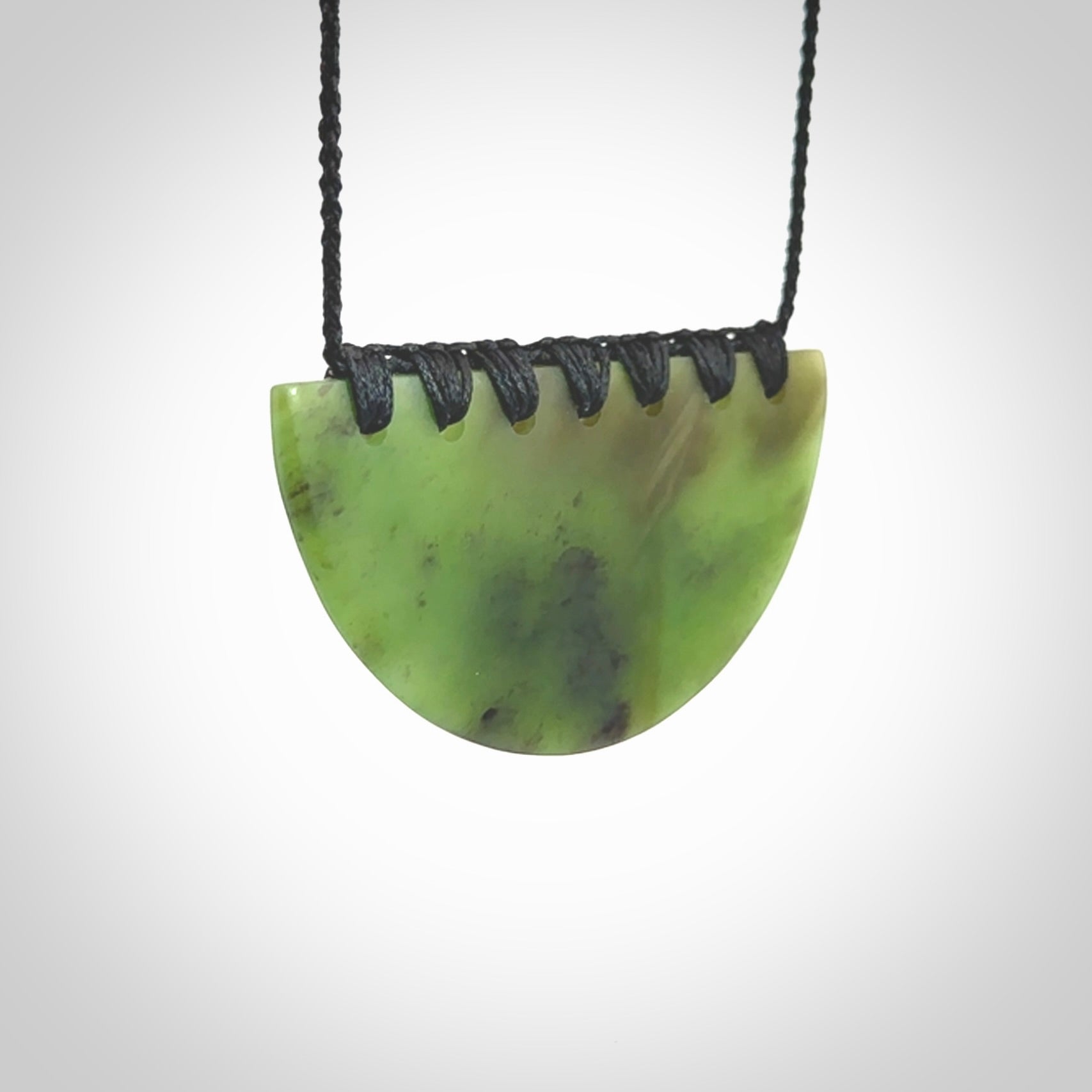 This picture shows a hand carved jade contemporary half-shield pendant. It is a deep green colour. This is a wonderful piece of jewellery. The cord is hand plaited and adjustable so that you can position the pendant where it suits you best. This piece was carved for us by Ric Moor. Delivery is free worldwide.