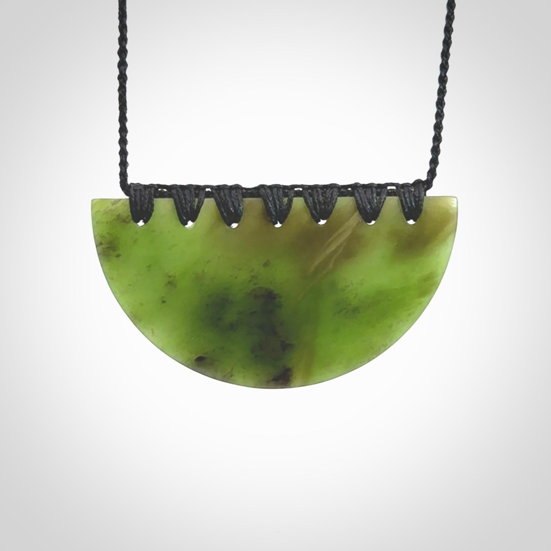 This picture shows a hand carved jade contemporary half-shield pendant. It is a deep green colour. This is a wonderful piece of jewellery. The cord is hand plaited and adjustable so that you can position the pendant where it suits you best. This piece was carved for us by Ric Moor. Delivery is free worldwide.