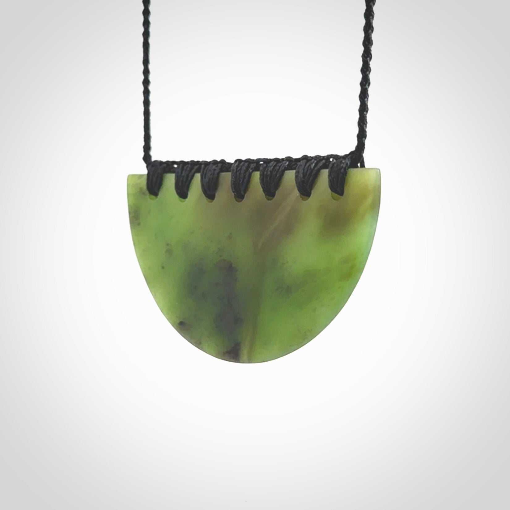 This picture shows a hand carved jade contemporary half-shield pendant. It is a deep green colour. This is a wonderful piece of jewellery. The cord is hand plaited and adjustable so that you can position the pendant where it suits you best. This piece was carved for us by Ric Moor. Delivery is free worldwide.