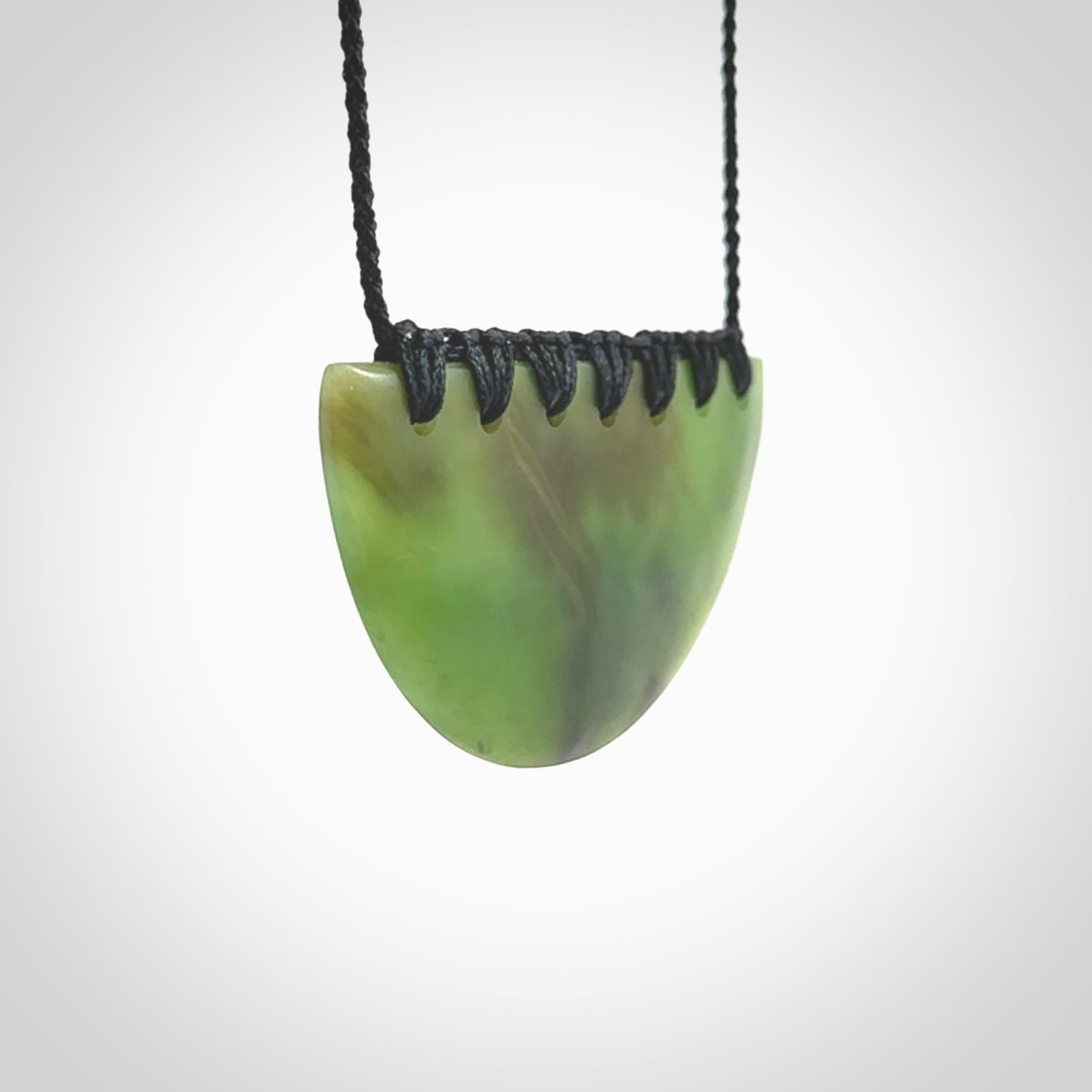 This picture shows a hand carved jade contemporary half-shield pendant. It is a deep green colour. This is a wonderful piece of jewellery. The cord is hand plaited and adjustable so that you can position the pendant where it suits you best. This piece was carved for us by Ric Moor. Delivery is free worldwide.