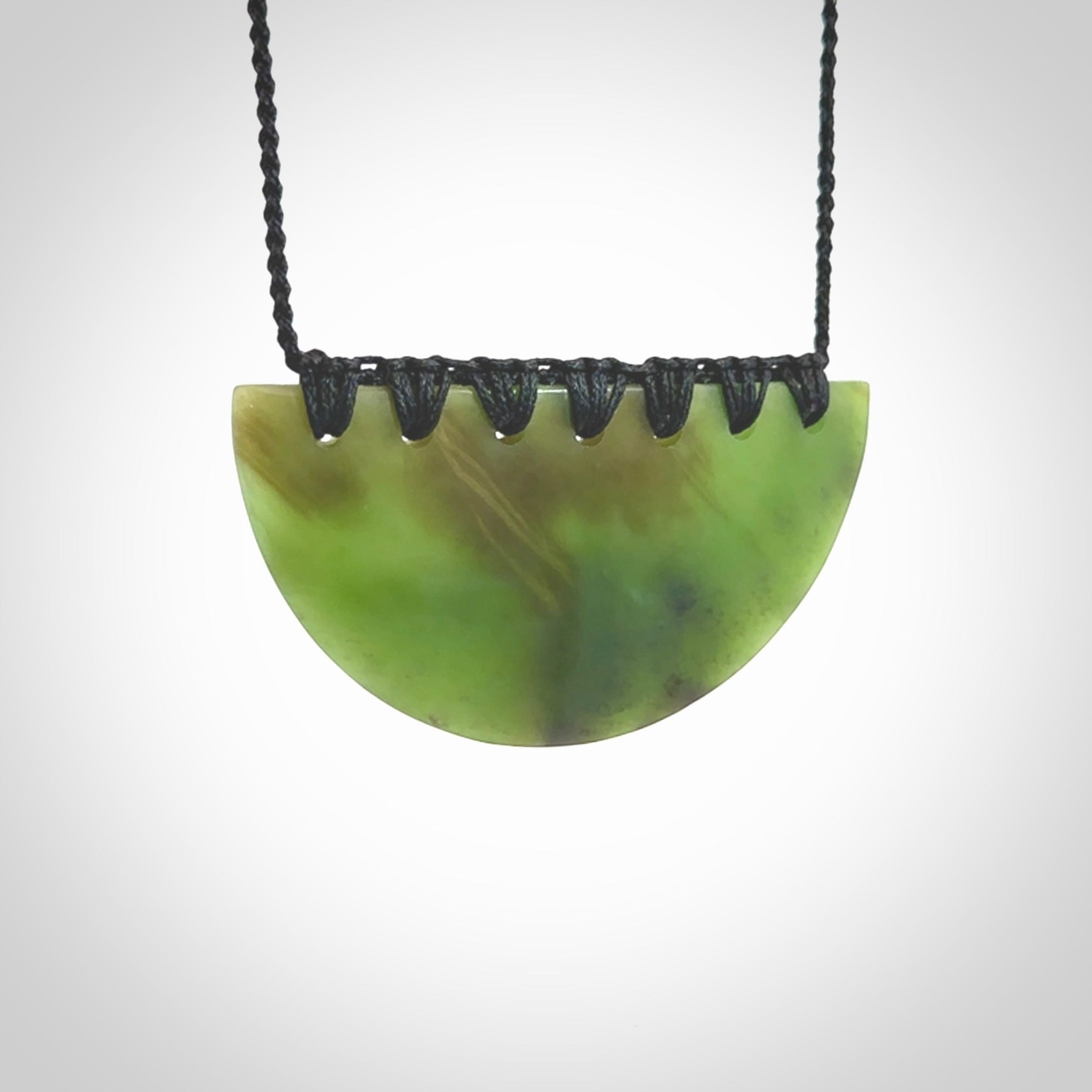 This picture shows a hand carved jade contemporary half-shield pendant. It is a deep green colour. This is a wonderful piece of jewellery. The cord is hand plaited and adjustable so that you can position the pendant where it suits you best. This piece was carved for us by Ric Moor. Delivery is free worldwide.