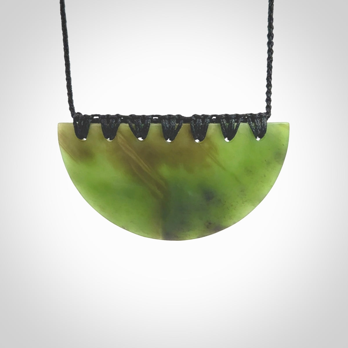 This picture shows a hand carved jade contemporary half-shield pendant. It is a deep green colour. This is a wonderful piece of jewellery. The cord is hand plaited and adjustable so that you can position the pendant where it suits you best. This piece was carved for us by Ric Moor. Delivery is free worldwide.