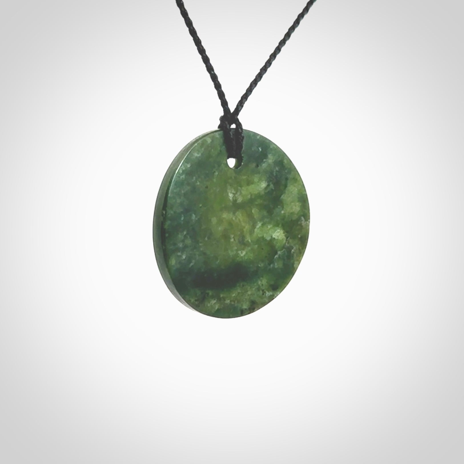 A lovely disc design with cupping on one side and the lightly convex form on the other - a little feature that captures the light and gives the piece a sense of movement and form. Hand made from New Zealand Jade by Ric Moor. Delivered with an adjustable black cord.&nbsp;