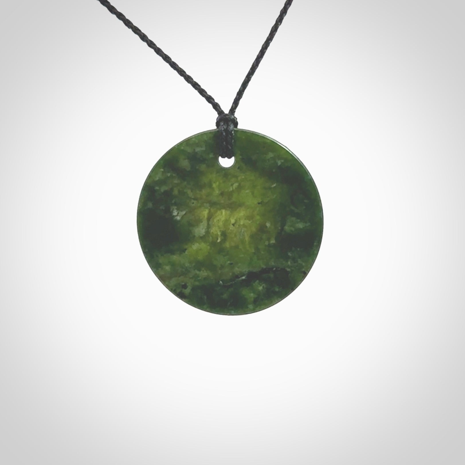 A lovely disc design with cupping on one side and the lightly convex form on the other - a little feature that captures the light and gives the piece a sense of movement and form. Hand made from New Zealand Jade by Ric Moor. Delivered with an adjustable black cord.&nbsp;