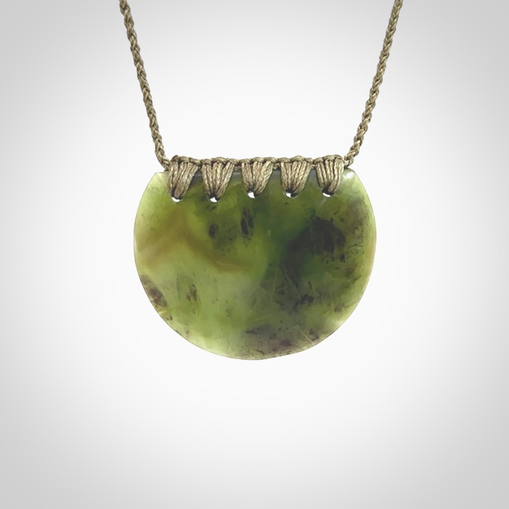 This piece is a disc pendant, hand carved for us by Ric Moor from a lovely milky green piece of New Zealand jade. It is suspended on a olive coloured braided cord that is length adjustable.