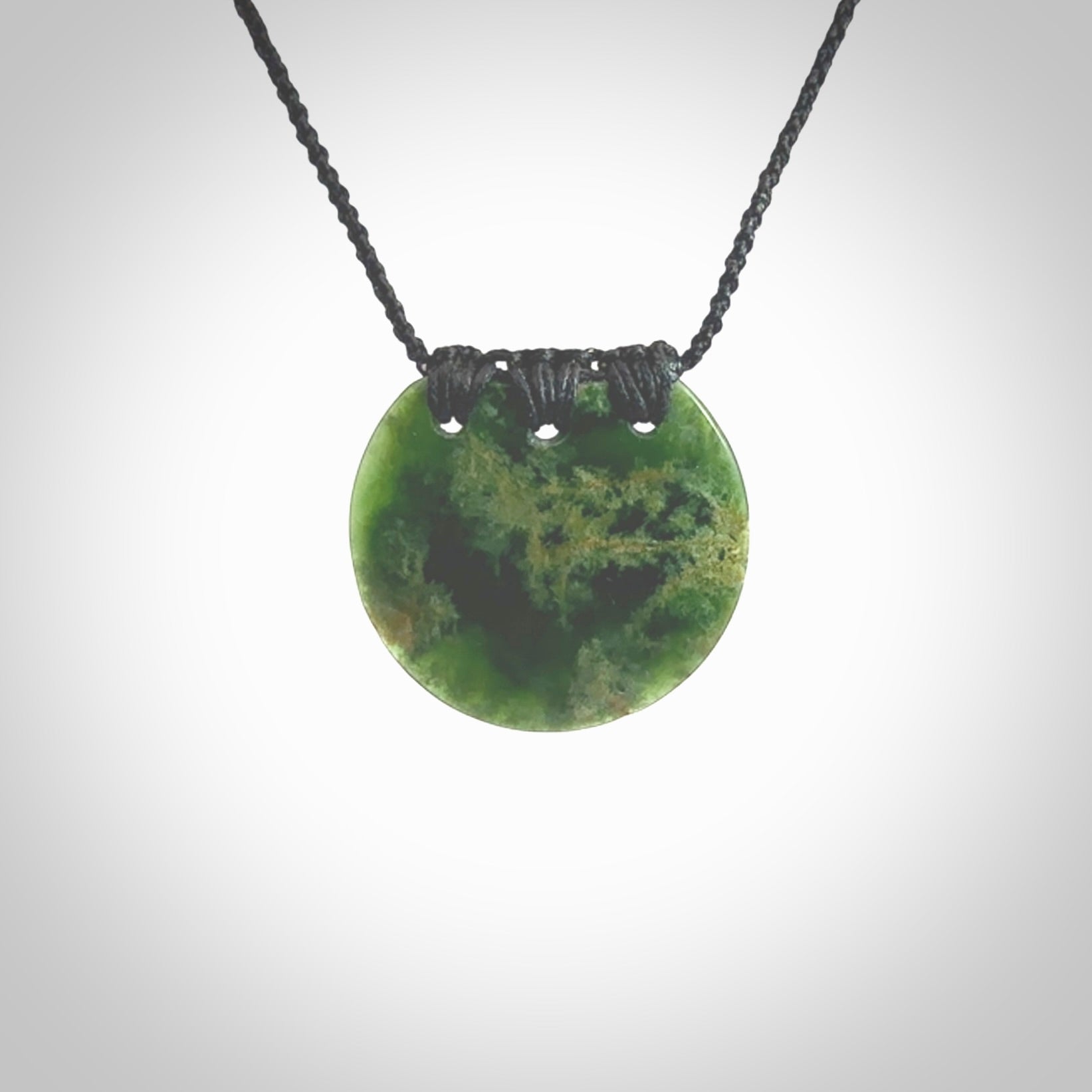 This piece is a medium sized, oval round, disc pendant. It was carved for us by Ric Moor from a lovely deep green and orange piece of New Zealand flower jade. It is suspended on an black coloured braided cord that is length adjustable.