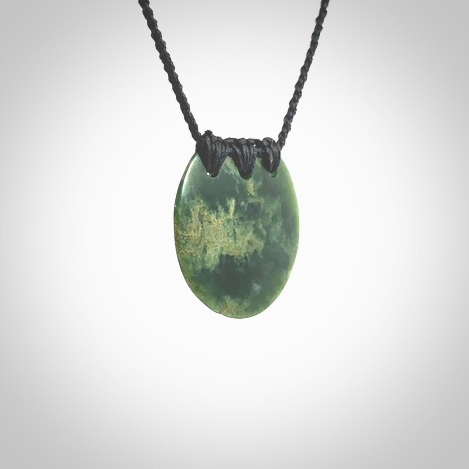 This piece is a medium sized, oval round, disc pendant. It was carved for us by Ric Moor from a lovely deep green and orange piece of New Zealand flower jade. It is suspended on an black coloured braided cord that is length adjustable.