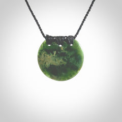 This piece is a medium sized, oval round, disc pendant. It was carved for us by Ric Moor from a lovely deep green and orange piece of New Zealand flower jade. It is suspended on an black coloured braided cord that is length adjustable.