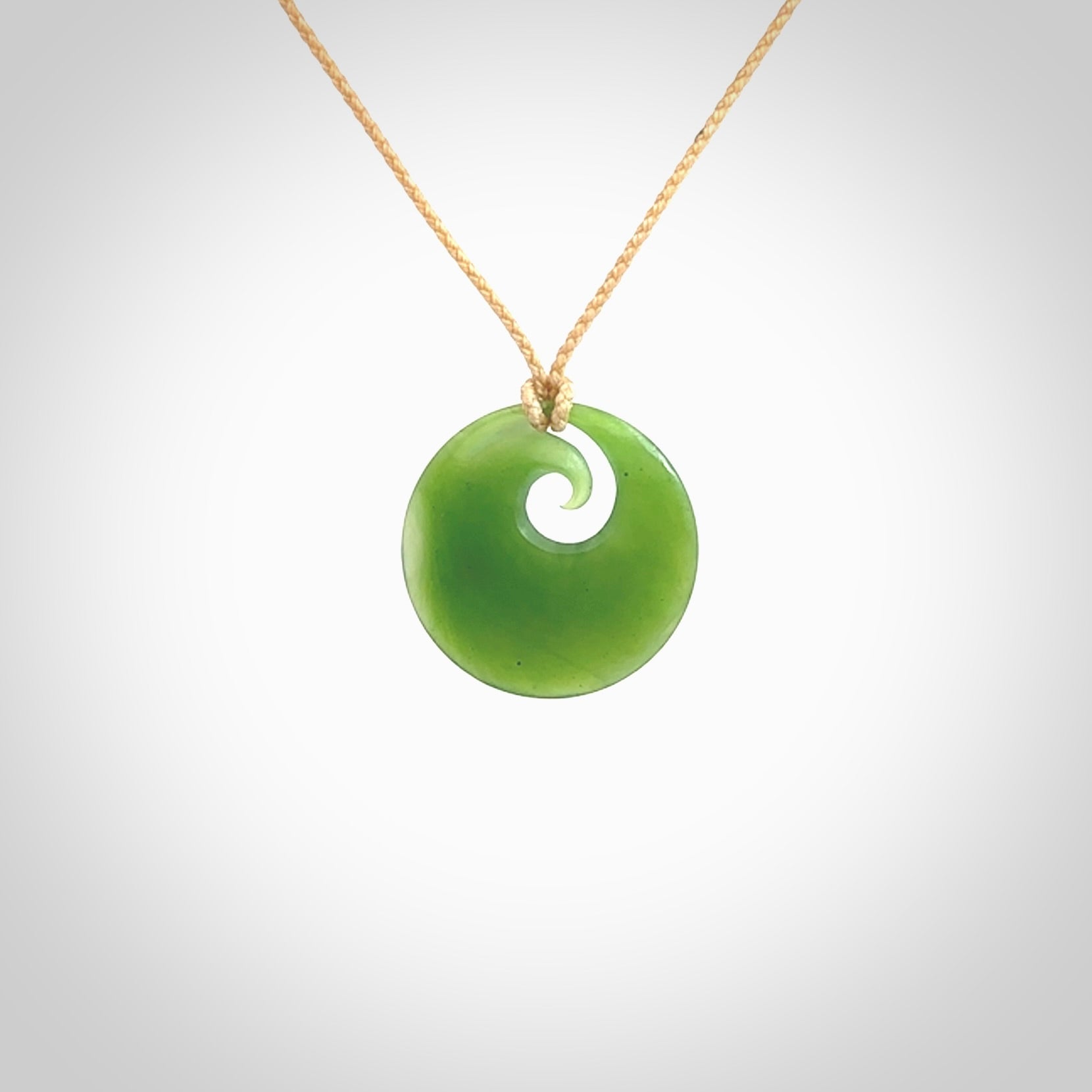 This is a small light green New Zealand Inanga jade koru pendant. We have bound this with a fine beige coloured cord necklace. The necklace is adjustable so you can position the piece where it suits you the best.