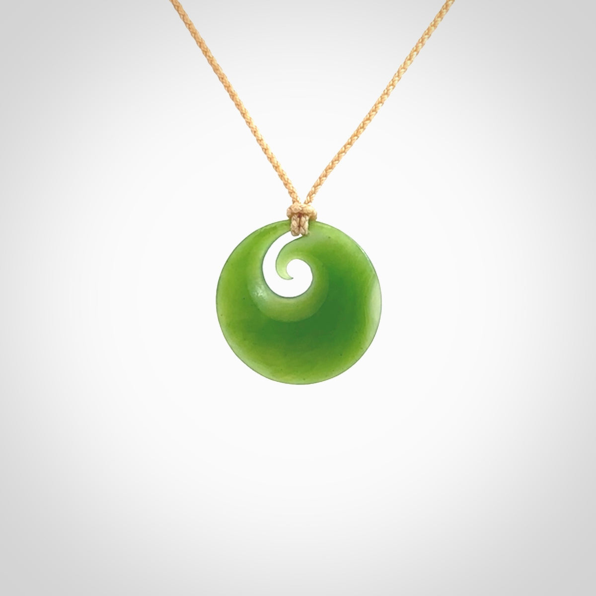 This is a small light green New Zealand Inanga jade koru pendant. We have bound this with a fine beige coloured cord necklace. The necklace is adjustable so you can position the piece where it suits you the best.