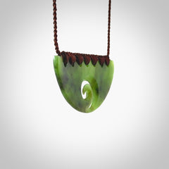 This picture shows a hand carved jade half-shield with Koru pendant. It is a semi-translucent green colour. This is a wonderful piece of jewellery. The cord is hand plaited and adjustable so that you can position the pendant where it suits you best. This piece was carved for us by Ric Moor. Delivery is free worldwide.