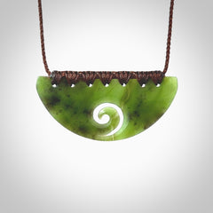 This picture shows a hand carved jade half-shield with Koru pendant. It is a semi-translucent green colour. This is a wonderful piece of jewellery. The cord is hand plaited and adjustable so that you can position the pendant where it suits you best. This piece was carved for us by Ric Moor. Delivery is free worldwide.