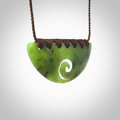 This picture shows a hand carved jade half-shield with Koru pendant. It is a semi-translucent green colour. This is a wonderful piece of jewellery. The cord is hand plaited and adjustable so that you can position the pendant where it suits you best. This piece was carved for us by Ric Moor. Delivery is free worldwide.