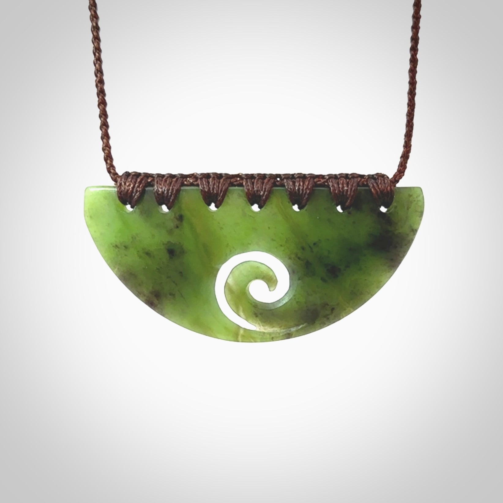 This picture shows a hand carved jade half-shield with Koru pendant. It is a semi-translucent green colour. This is a wonderful piece of jewellery. The cord is hand plaited and adjustable so that you can position the pendant where it suits you best. This piece was carved for us by Ric Moor. Delivery is free worldwide.