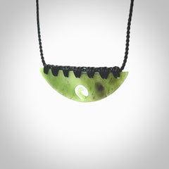 This picture shows a hand carved jade half-shield with Koru pendant. It is a semi-translucent green colour. This is a wonderful piece of jewellery. The cord is hand plaited and adjustable so that you can position the pendant where it suits you best. This piece was carved for us by Ric Moor. Delivery is free worldwide.