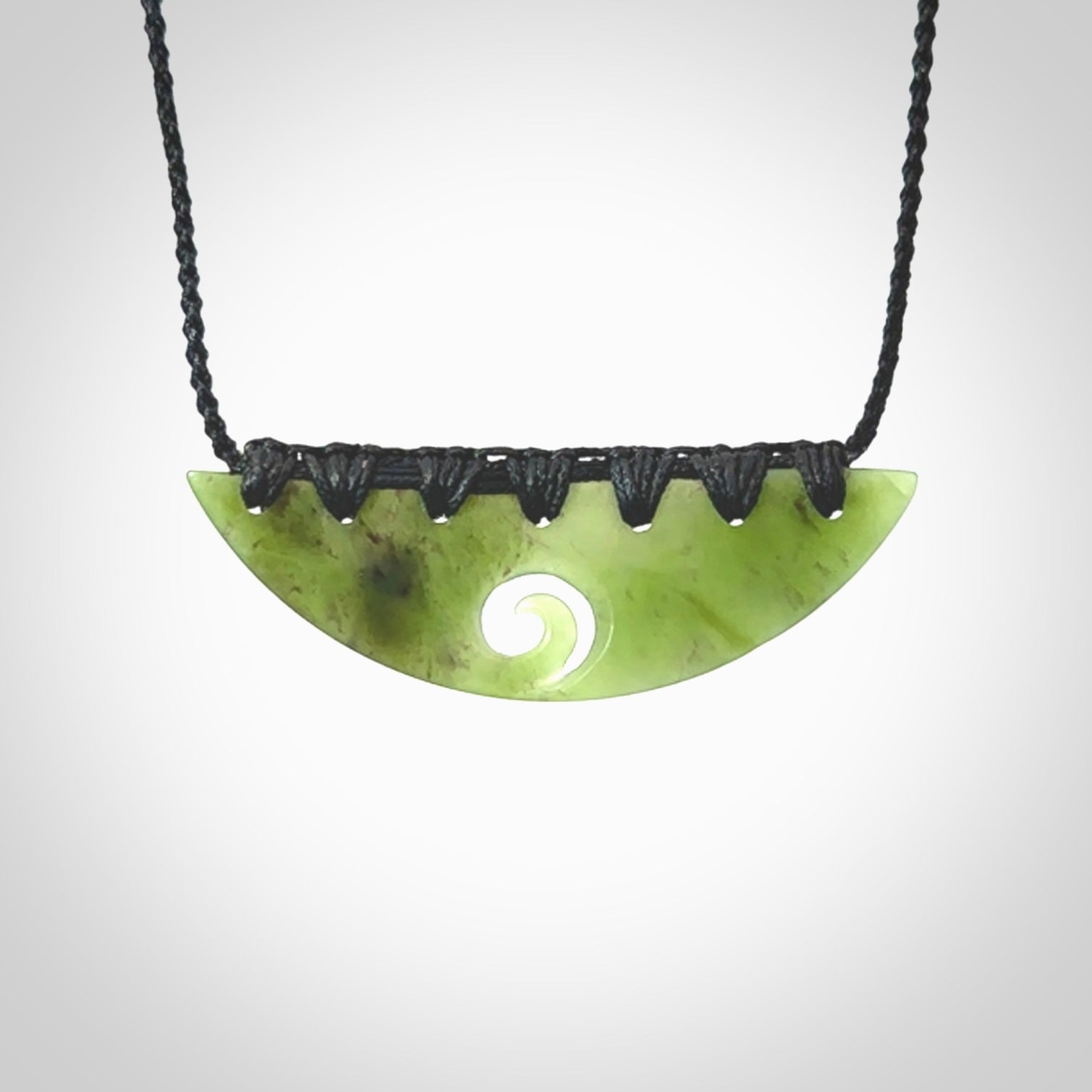 This picture shows a hand carved jade half-shield with Koru pendant. It is a semi-translucent green colour. This is a wonderful piece of jewellery. The cord is hand plaited and adjustable so that you can position the pendant where it suits you best. This piece was carved for us by Ric Moor. Delivery is free worldwide.