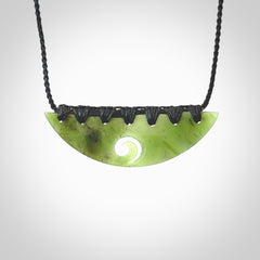 This picture shows a hand carved jade half-shield with Koru pendant. It is a semi-translucent green colour. This is a wonderful piece of jewellery. The cord is hand plaited and adjustable so that you can position the pendant where it suits you best. This piece was carved for us by Ric Moor. Delivery is free worldwide.