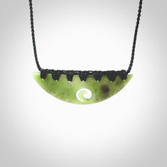 This picture shows a hand carved jade half-shield with Koru pendant. It is a semi-translucent green colour. This is a wonderful piece of jewellery. The cord is hand plaited and adjustable so that you can position the pendant where it suits you best. This piece was carved for us by Ric Moor. Delivery is free worldwide.