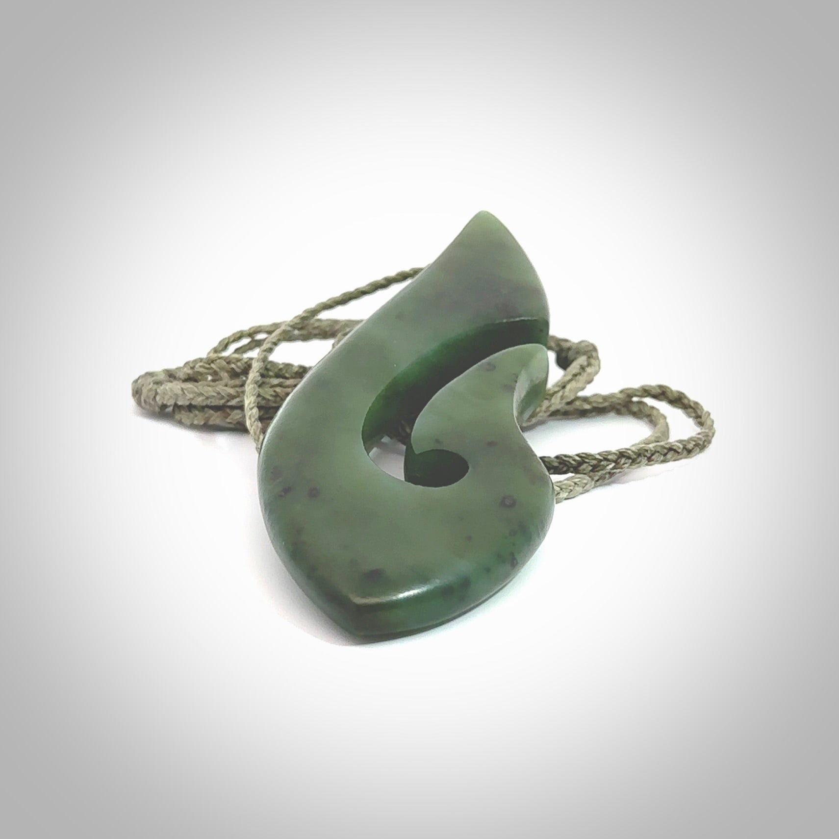 A hand carved hook design pendant, carved in New Zealand Kawakawa Jade. The colour is a beautiful deep green. The cord is khaki green and is length adjustable. Hand made by Rueben Tipene. Delivered with Express courier in a woven kete pouch.