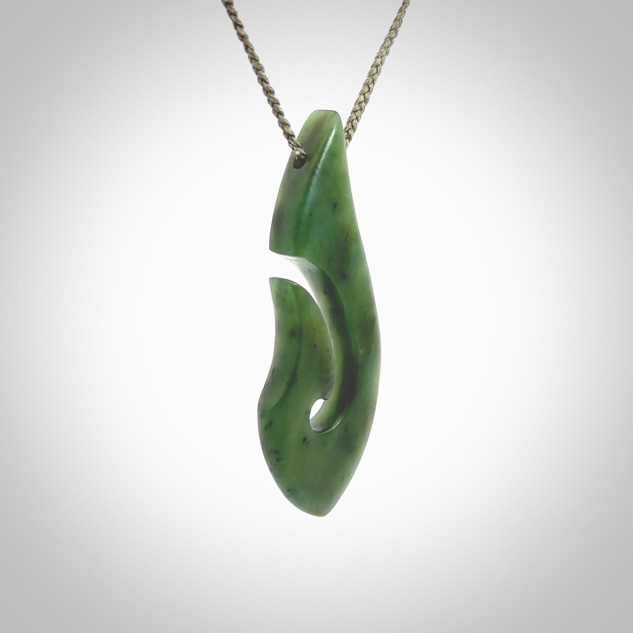 A hand carved hook design pendant, carved in New Zealand Kawakawa Jade. The colour is a beautiful deep green. The cord is khaki green and is length adjustable. Hand made by Rueben Tipene. Delivered with Express courier in a woven kete pouch.