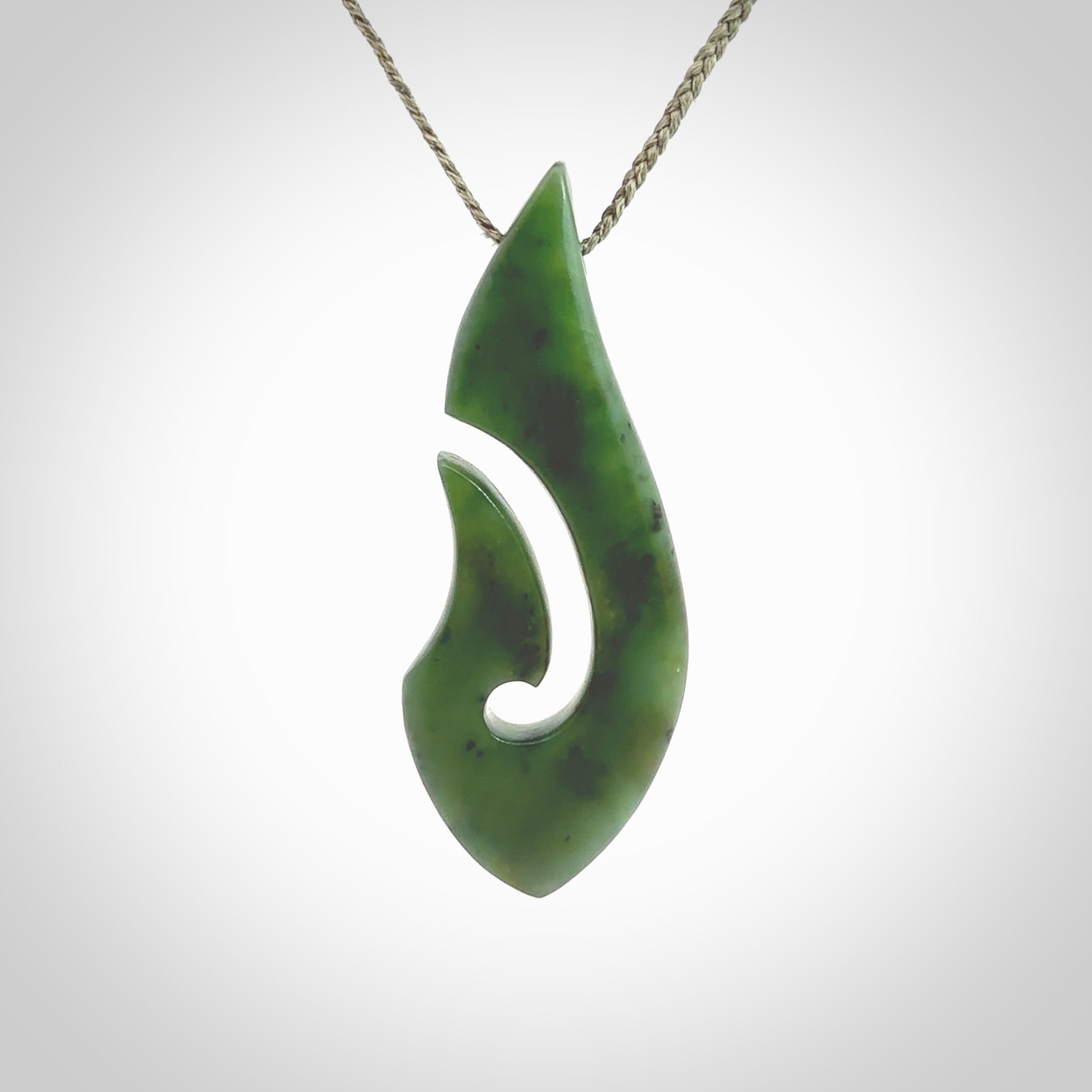 A hand carved hook design pendant, carved in New Zealand Kawakawa Jade. The colour is a beautiful deep green. The cord is khaki green and is length adjustable. Hand made by Rueben Tipene. Delivered with Express courier in a woven kete pouch.