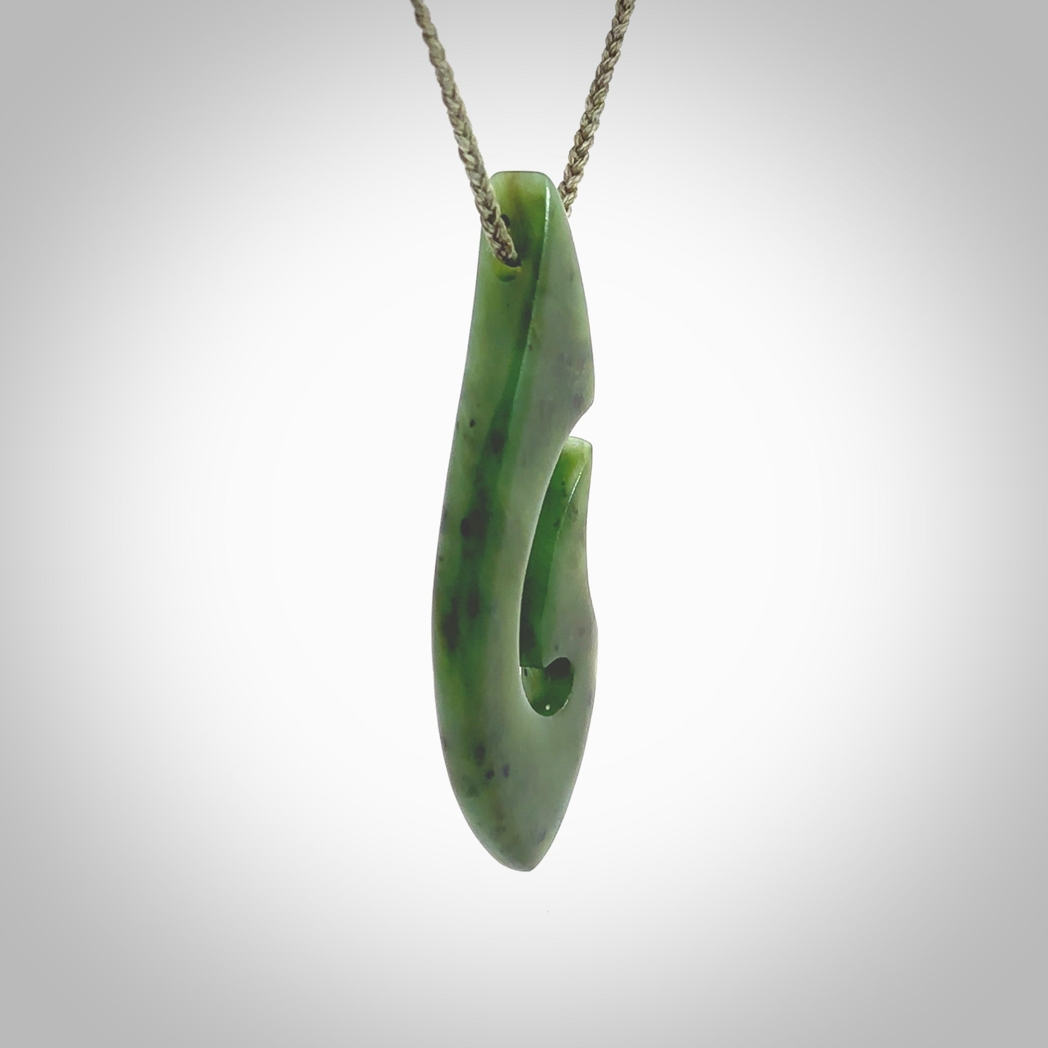 A hand carved hook design pendant, carved in New Zealand Kawakawa Jade. The colour is a beautiful deep green. The cord is khaki green and is length adjustable. Hand made by Rueben Tipene. Delivered with Express courier in a woven kete pouch.