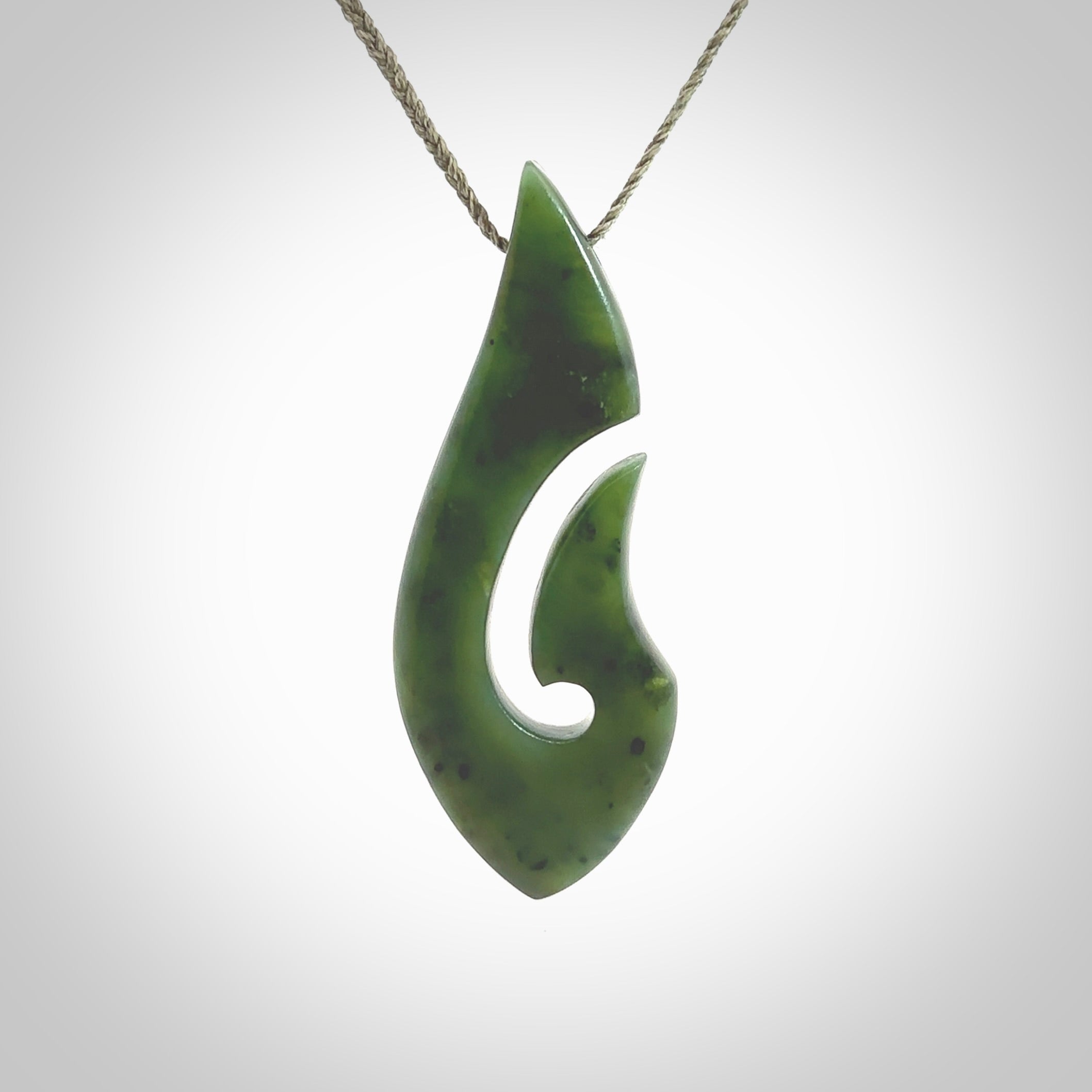 A hand carved hook design pendant, carved in New Zealand Kawakawa Jade. The colour is a beautiful deep green. The cord is khaki green and is length adjustable. Hand made by Rueben Tipene. Delivered with Express courier in a woven kete pouch.