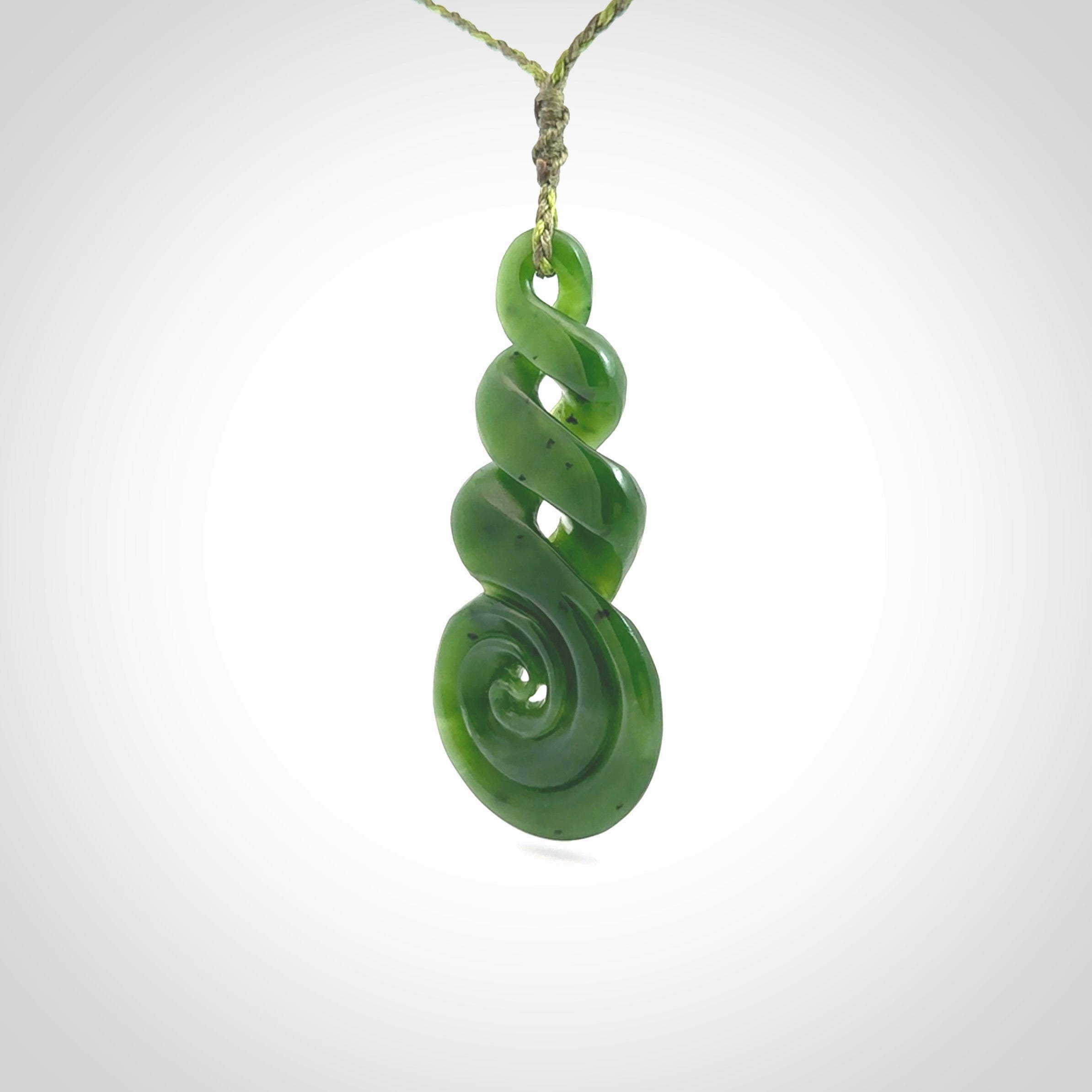 Ross Crump triple twist with koru pendant. Hand carved from rare New Zealand jade this is a beautiful pounamu pendant. The cord is 4-plait in a grass green and khaki colour and is length adjustable. It has a floret in khaki green. It is a delicate and very beautiful greenstone pendant. For sale online by NZ Pacific.