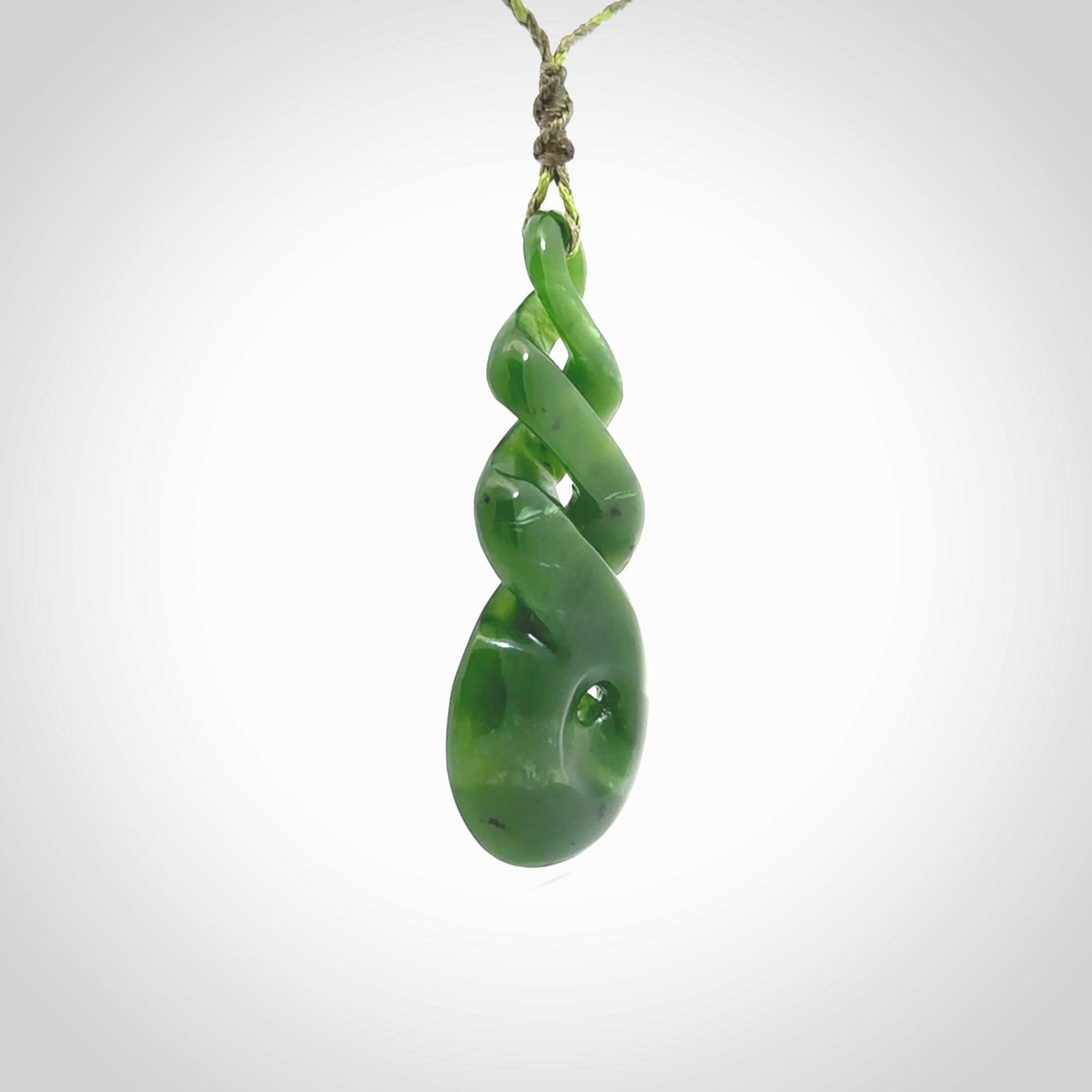 Ross Crump triple twist with koru pendant. Hand carved from rare New Zealand jade this is a beautiful pounamu pendant. The cord is 4-plait in a grass green and khaki colour and is length adjustable. It has a floret in khaki green. It is a delicate and very beautiful greenstone pendant. For sale online by NZ Pacific.