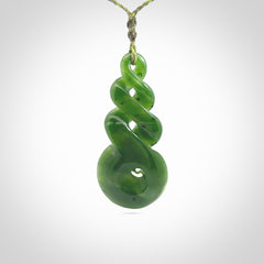 Ross Crump triple twist with koru pendant. Hand carved from rare New Zealand jade this is a beautiful pounamu pendant. The cord is 4-plait in a grass green and khaki colour and is length adjustable. It has a floret in khaki green. It is a delicate and very beautiful greenstone pendant. For sale online by NZ Pacific.