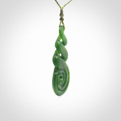 Ross Crump triple twist with koru pendant. Hand carved from rare New Zealand jade this is a beautiful pounamu pendant. The cord is 4-plait in a grass green and khaki colour and is length adjustable. It has a floret in khaki green. It is a delicate and very beautiful greenstone pendant. For sale online by NZ Pacific.