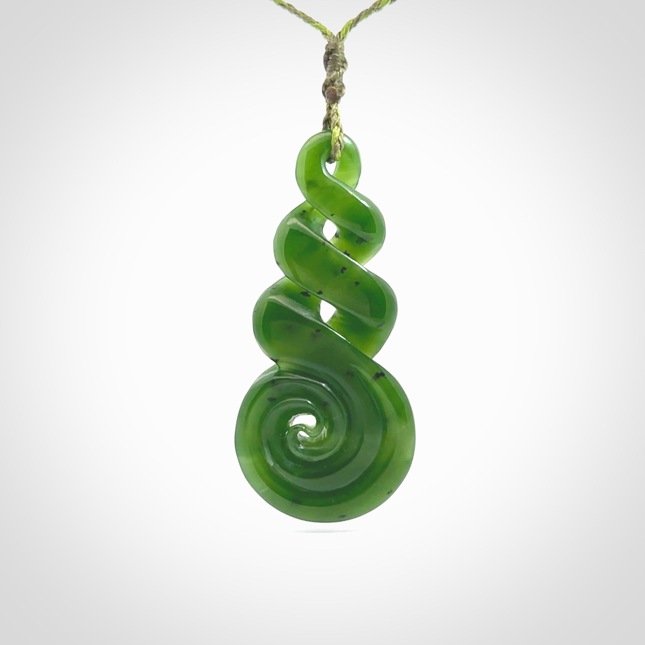 Ross Crump triple twist with koru pendant. Hand carved from rare New Zealand jade this is a beautiful pounamu pendant. The cord is 4-plait in a grass green and khaki colour and is length adjustable. It has a floret in khaki green. It is a delicate and very beautiful greenstone pendant. For sale online by NZ Pacific.