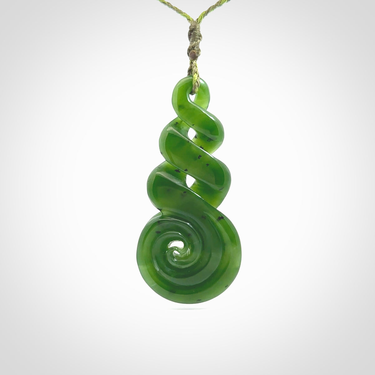 Ross Crump triple twist with koru pendant. Hand carved from rare New Zealand jade this is a beautiful pounamu pendant. The cord is 4-plait in a grass green and khaki colour and is length adjustable. It has a floret in khaki green. It is a delicate and very beautiful greenstone pendant. For sale online by NZ Pacific.