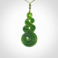 Ross Crump triple twist with koru pendant. Hand carved from rare New Zealand jade this is a beautiful pounamu pendant. The cord is 4-plait in a grass green and khaki colour and is length adjustable. It has a floret in khaki green. It is a delicate and very beautiful greenstone pendant. For sale online by NZ Pacific.