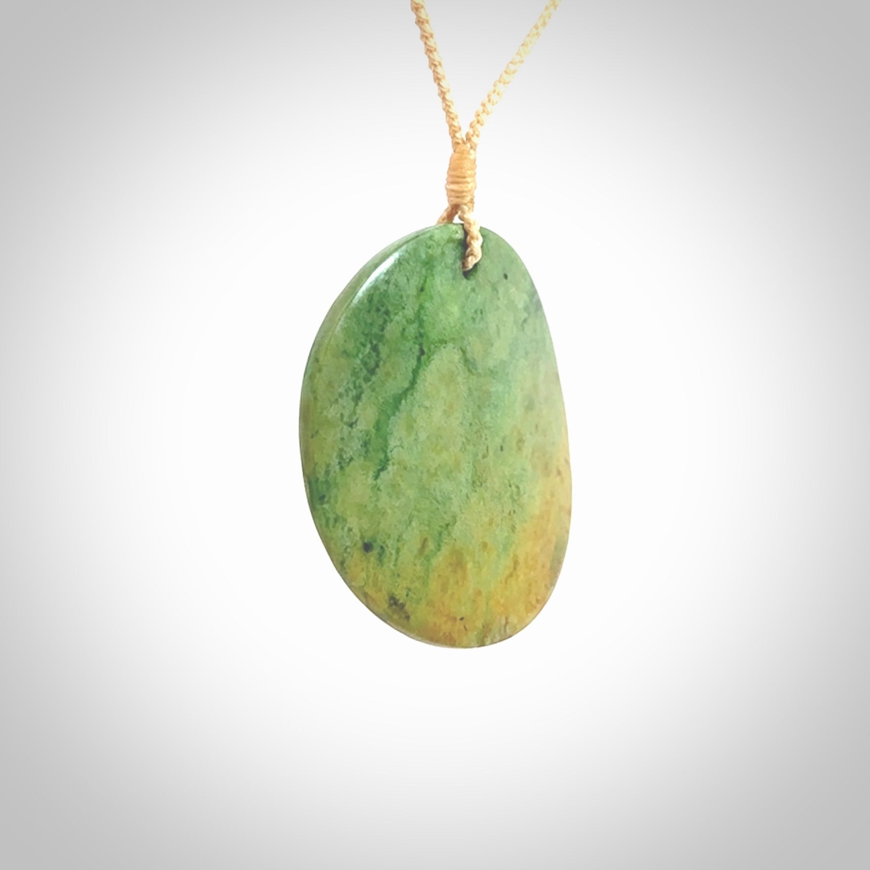 This piece is a large oval round, disc pendant. It was carved for us by Ric Moor from a lovely orange and green piece of New Zealand flower jade. It is suspended on a beige coloured braided cord that is length adjustable.