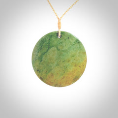 This piece is a large oval round, disc pendant. It was carved for us by Ric Moor from a lovely orange and green piece of New Zealand flower jade. It is suspended on a beige coloured braided cord that is length adjustable.