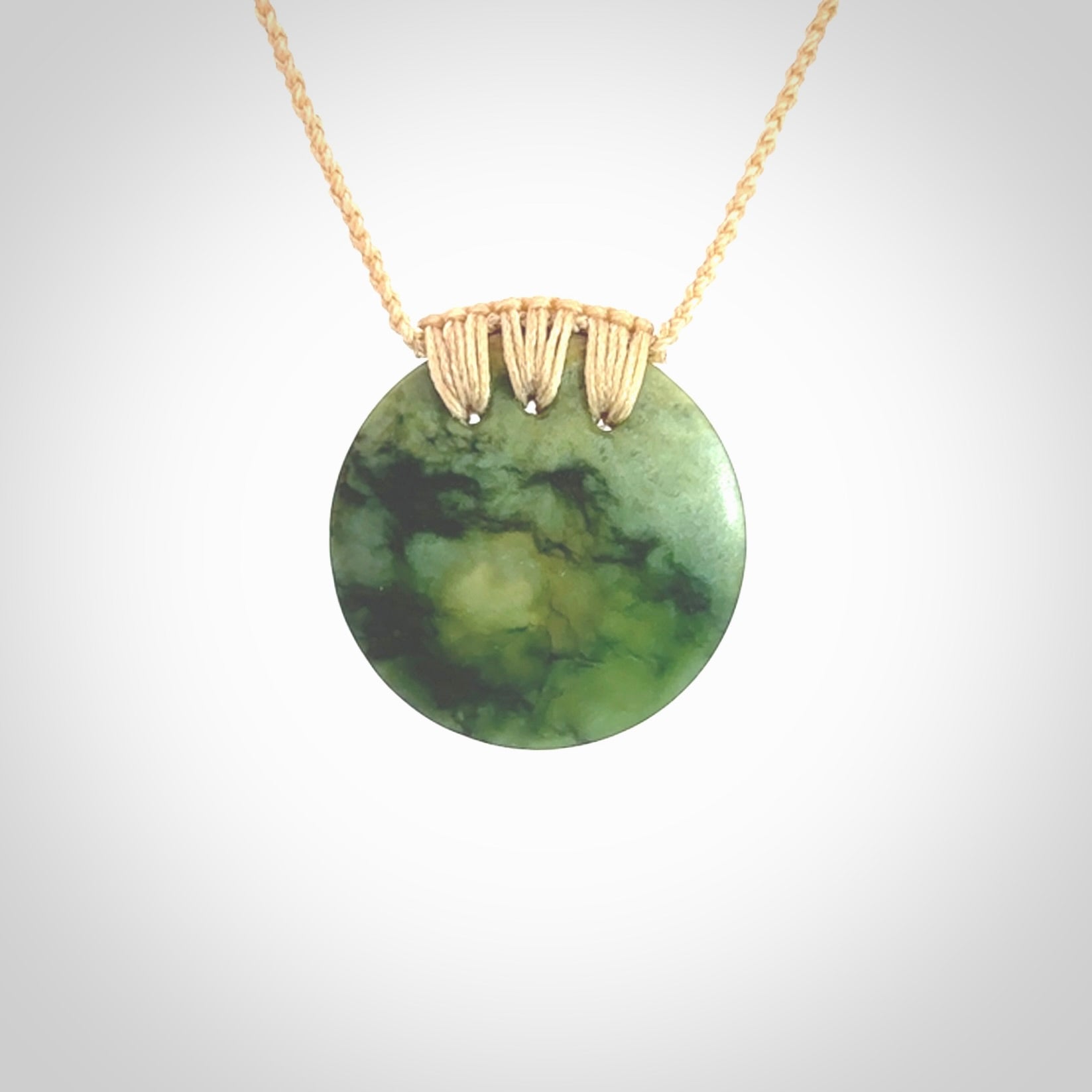 This piece is a medium sized cupped disc pendant. It was carved for us by Ric Moor from a lovely deep and milky green piece of New Zealand flower jade. It is suspended on a beige coloured braided cord that is length adjustable.