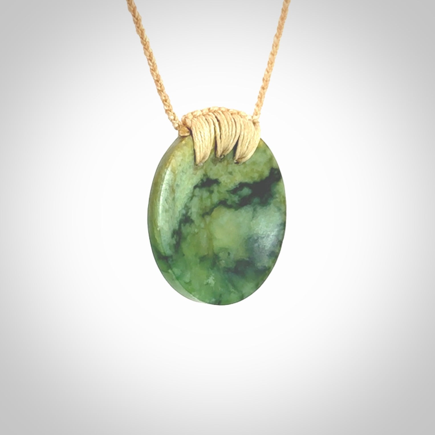 This piece is a medium sized cupped disc pendant. It was carved for us by Ric Moor from a lovely deep and milky green piece of New Zealand flower jade. It is suspended on a beige coloured braided cord that is length adjustable.