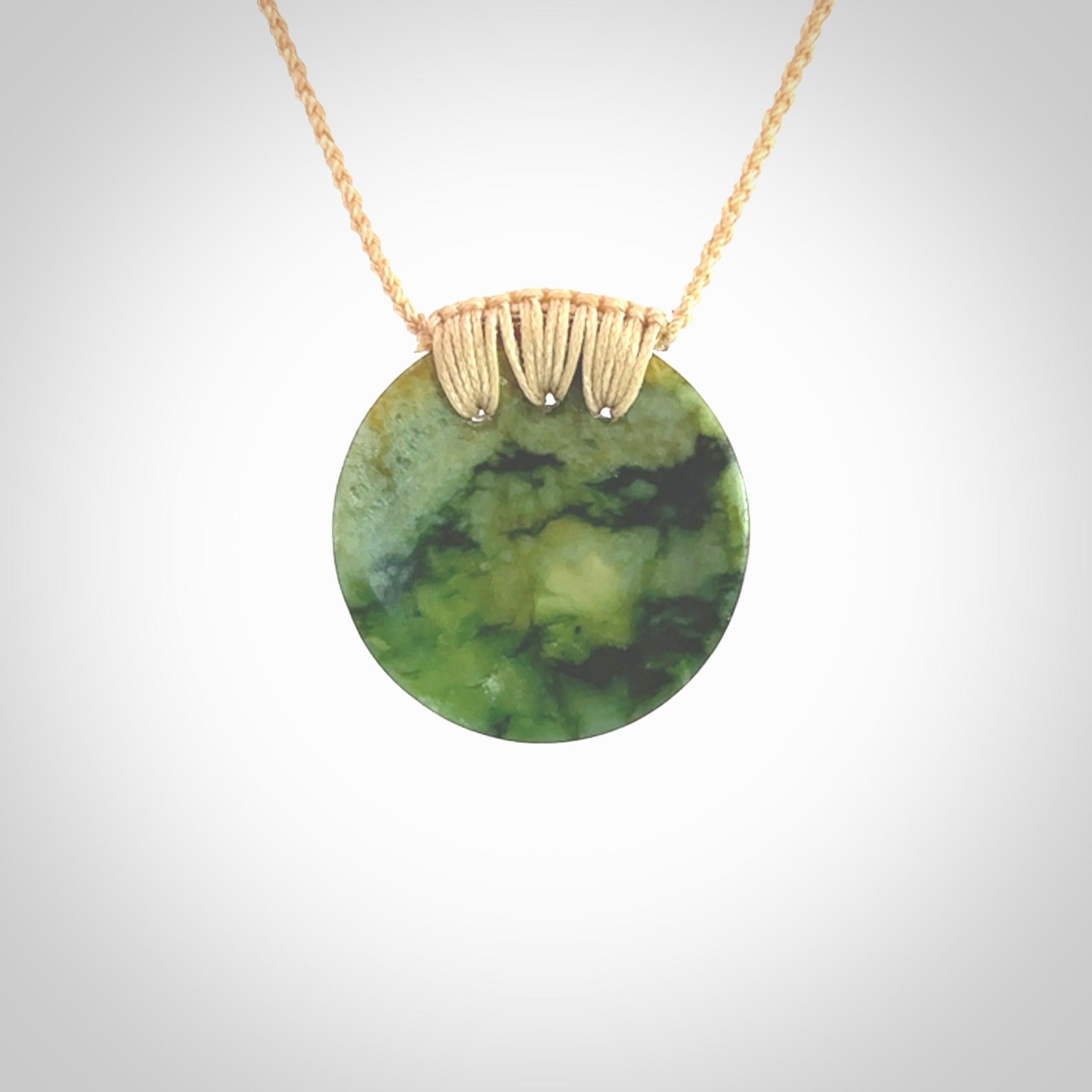 This piece is a medium sized cupped disc pendant. It was carved for us by Ric Moor from a lovely deep and milky green piece of New Zealand flower jade. It is suspended on a beige coloured braided cord that is length adjustable.