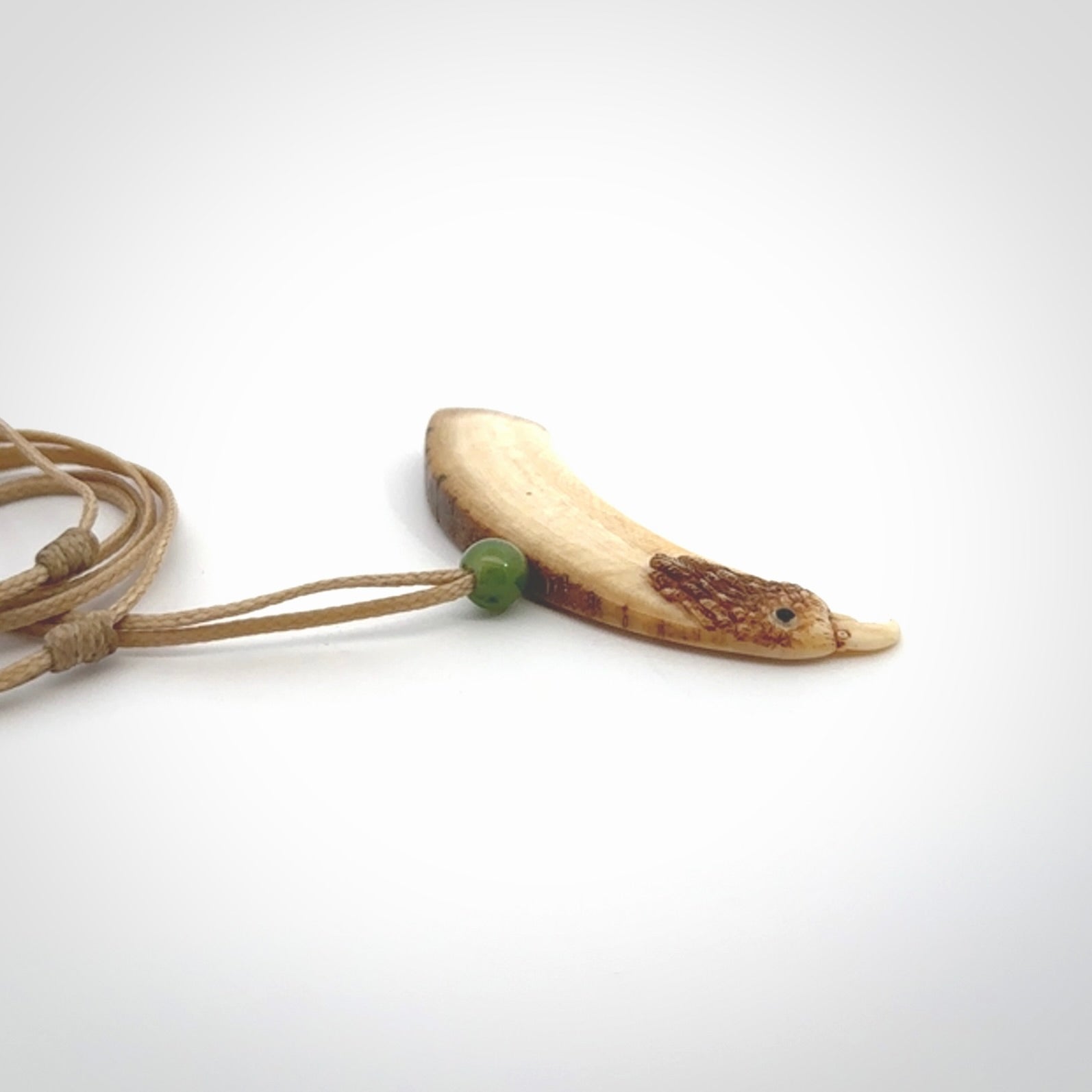 This is a hand carved deer antler bone kea bird head pendant. It is made from deer antler with jade bead. This is a medium sized necklace and is a very unique, one only, pendant that is a collectors piece. Hand carved by New Zealand artist, Sami. Provided with adjustable tan cord.