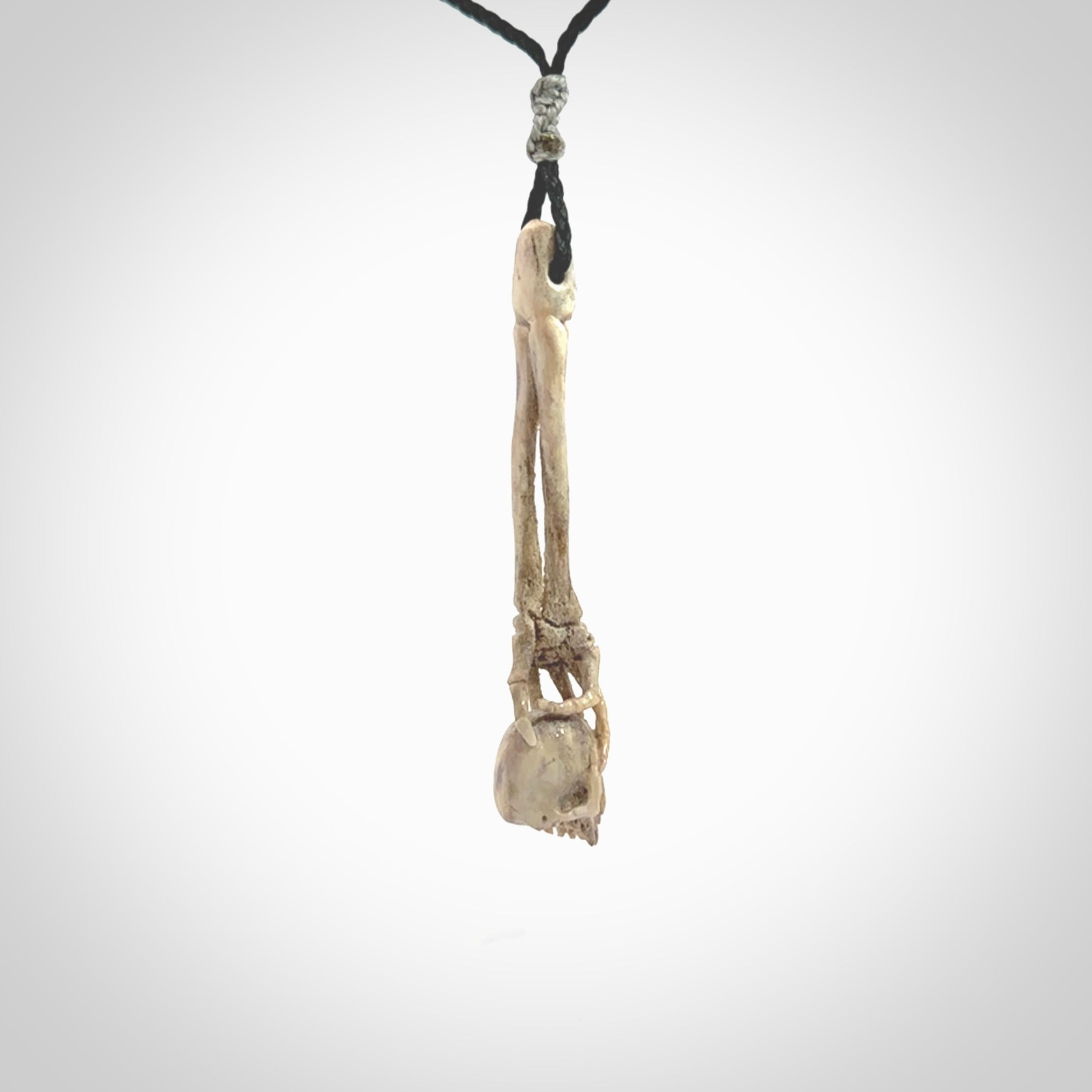 This picture shows a large sized Deer Antler Bone skull in skeleton hand pendant that we have hand carved. It is polished to a soft shine and is a very striking piece. The cord is a black colour and has a small grey floret binding just above the pendant.