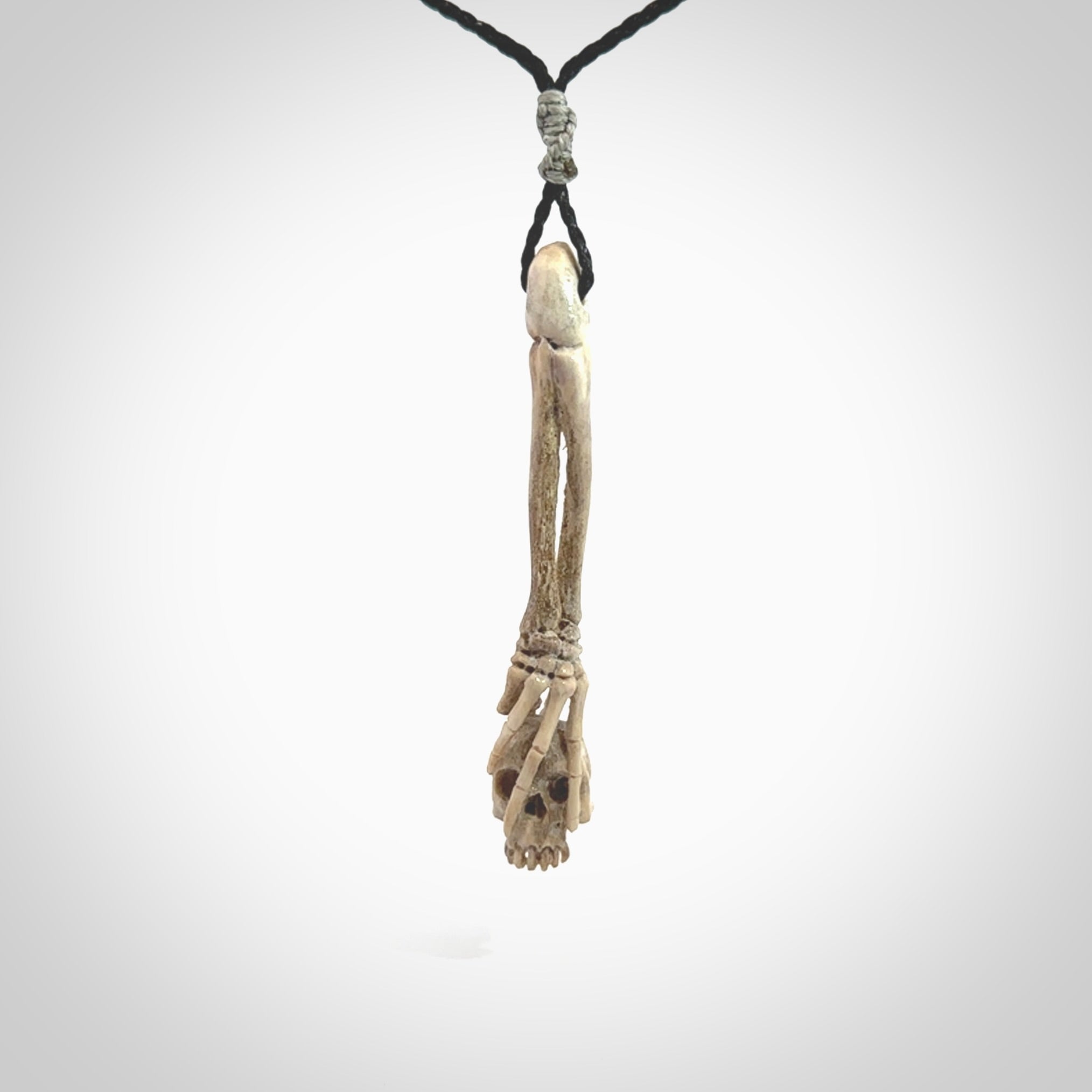 This picture shows a large sized Deer Antler Bone skull in skeleton hand pendant that we have hand carved. It is polished to a soft shine and is a very striking piece. The cord is a black colour and has a small grey floret binding just above the pendant.